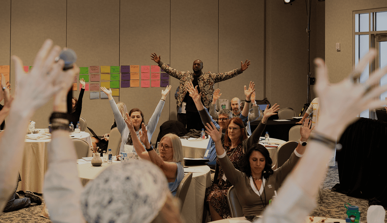 Executive Coach Darryll Stinson leading a high-energy corporate training or group workshop, with attendees actively participating by raising their hands.