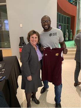 Darryll Stinson posing with a woman while holding a gift shirt after a speaking event