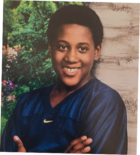 Childhood portrait of Darryll Stinson smiling with arms crossed outdoors