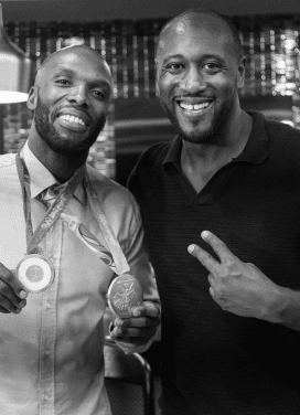 Darryll Stinson smiling with a colleague, holding medals at an event.